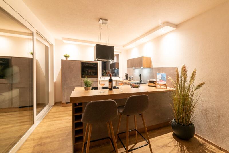 Ansicht der Küche abends, zwei Weingläser auf der Bar, zwei Barstühle davor