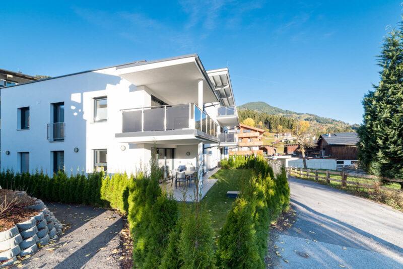 Man sieht das Haus im Sonnenschein, das Apartment 17 ist im ersten Stock. Man sieht Zufahrt zur Tiefgarage und Eingang